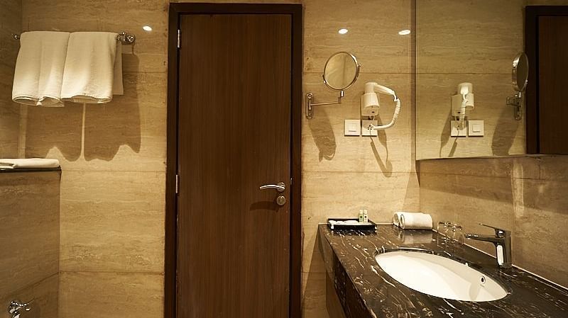 A bathroom with a sink, mirror, wooden door, and towel rack at The Hamuse Hotel, Kodaikanal.
