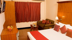 An executive bedroom with a king sized bed, curtains, chairs, a table, and lamps at the best resort in Bangalore  | Ramanashree California Resort