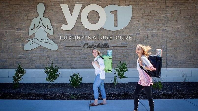 Yo1 signage in the background with 2 women walking with their backpacks during daytime