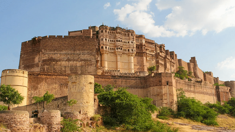 An exterior view of Mehrangarh Fort, towering majestically over the landscape, showcasing its impressive walls and intricate architectural details against the sky.