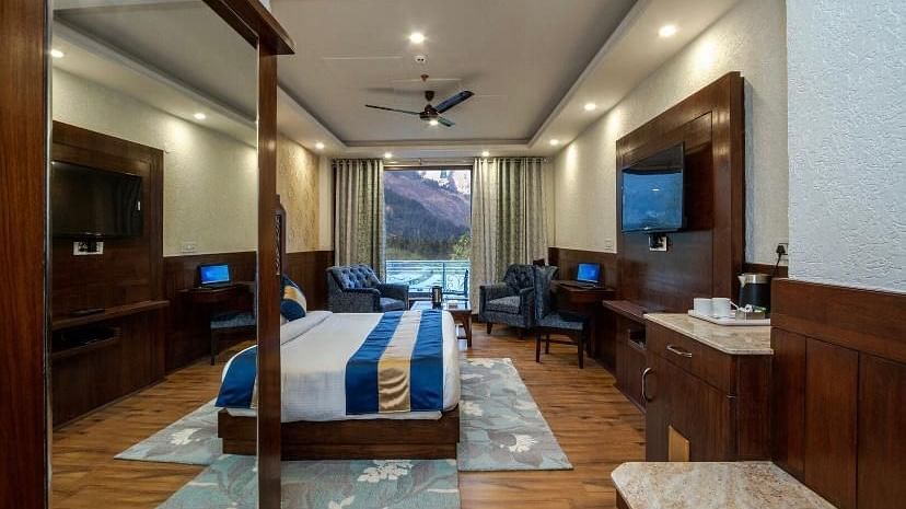  A spacious hotel room with a comfortable bed, a seating area, and a view of the mountains | DLS La Serene Manali