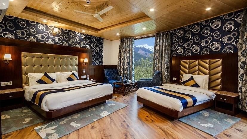 A spacious, luxurious hotel room with a king size bed, a twin bed, and a sitting area overlooking a scenic mountain view | DLS La Serene Manali