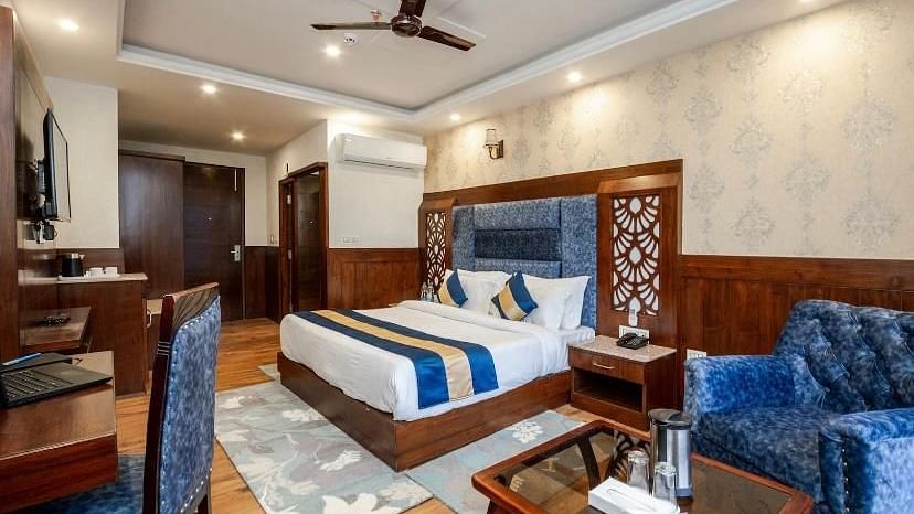 Image of a expansive hotel room featuring king size bed, a couch, wooden table and a work desk | DLS La Serene Manali