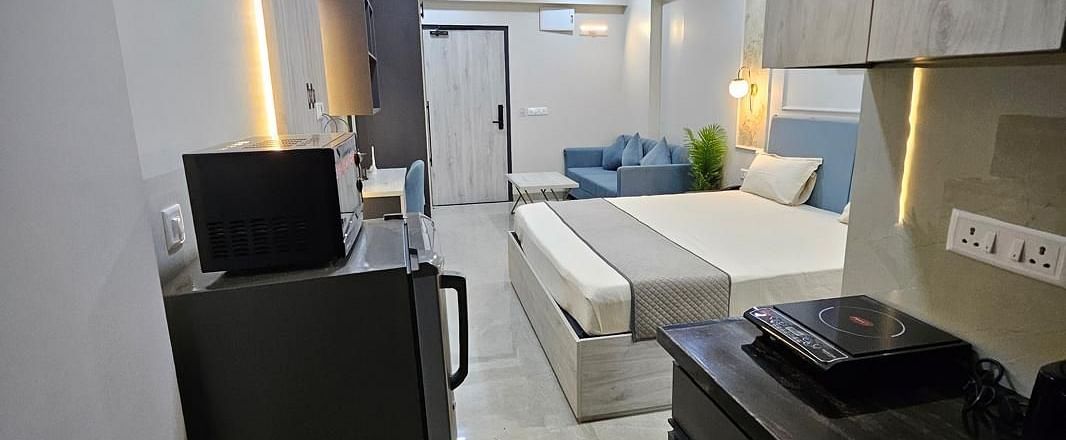 A view from the kitchen to the bedroom, featuring a counter with kitchen equipment, a fridge, and a bed in sight at Urban Suites by BluSalzz, Jaipur.