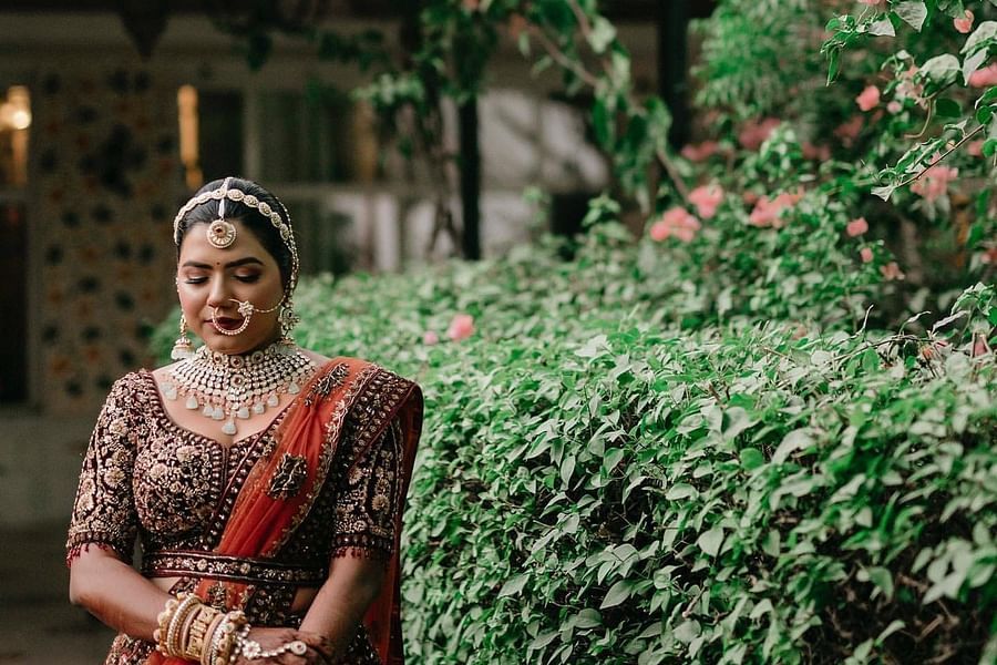 A bride in a richly embroidered lehenga poses gracefully in a lush garden, adorned with traditional jewelry and floral accents.- Umaid Palace - A Lakeside Heritage Palace Resort