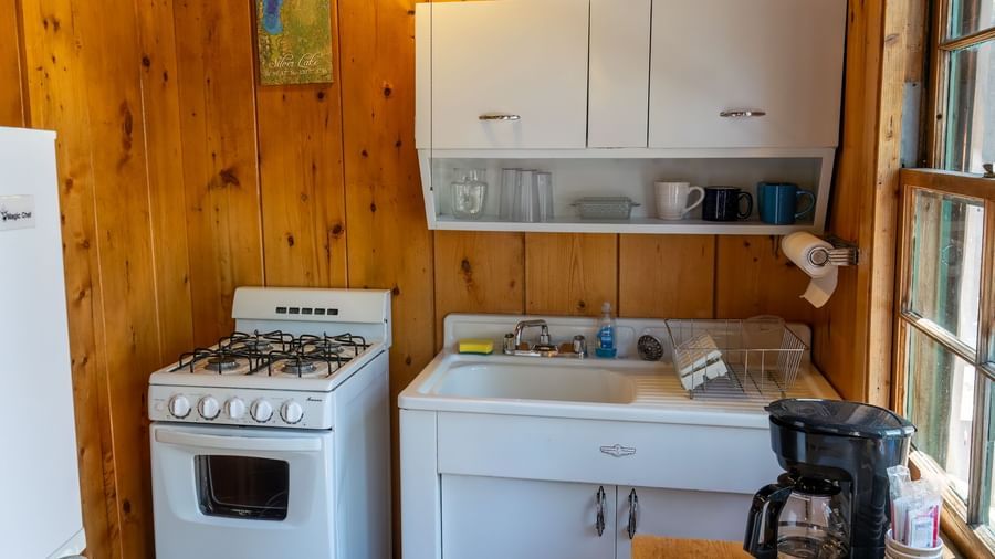 Small kitchen with stove, white cabinets, and coffee maker in a rustic cabin at Kit Carson Lodge.