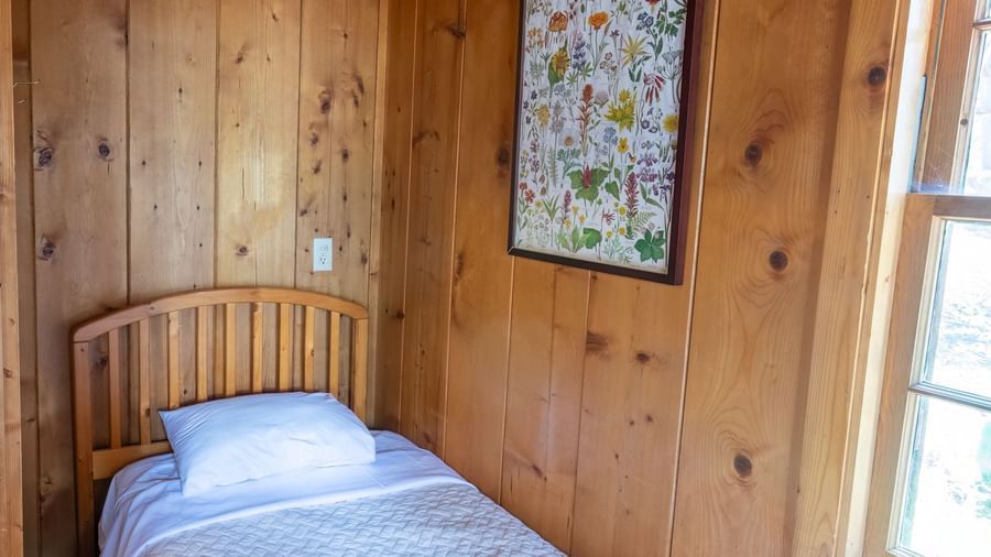 Small single bedroom with wooden interiors, window, and framed art in a quiet cabin at Kit Carson Lodge.