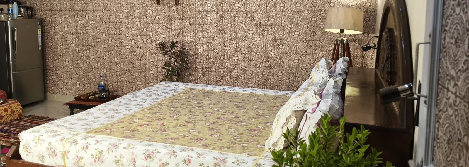 A neatly made double bed with patterned bedding, pillows, and wall hangings above the headboard at Jaypore360 Homestay in Jaipur.