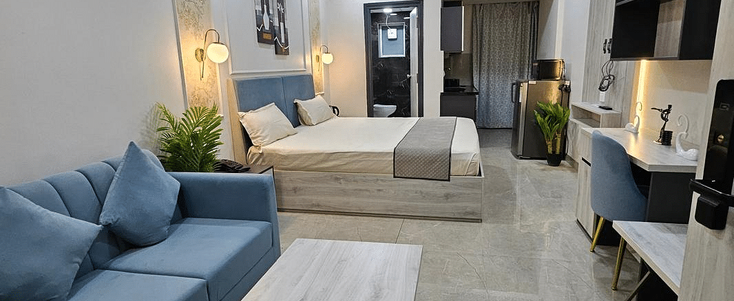 A side view of the spacious room with furniture and a table placed near the window, and a bed at the farthest end at Urban Suites by BluSalzz, Jaipur.