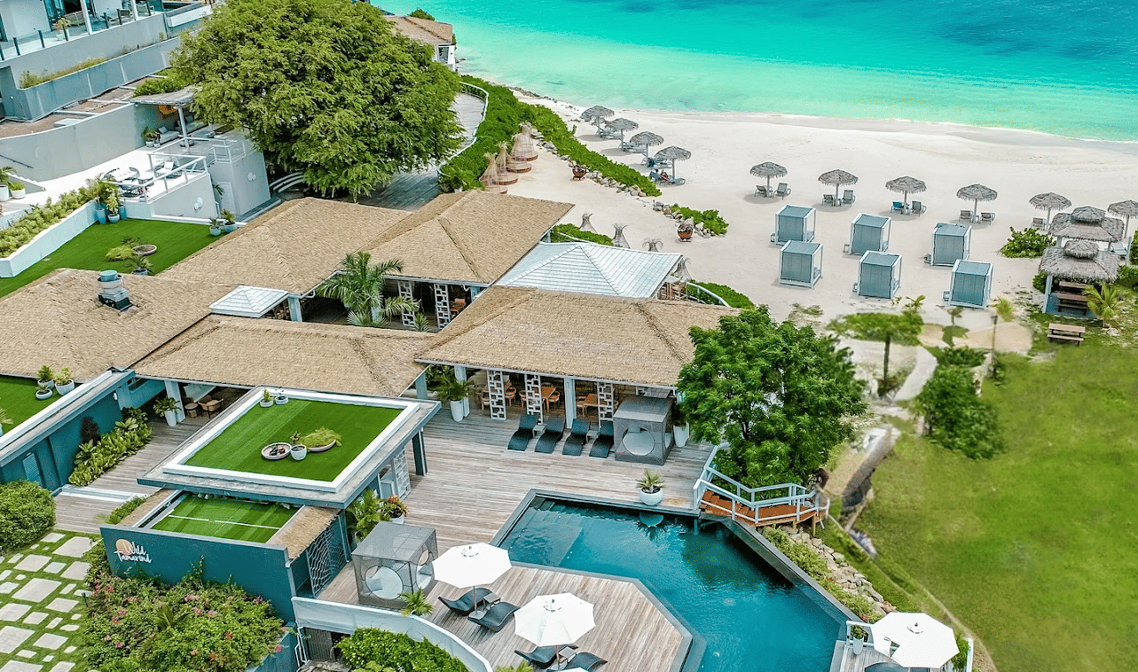 An aerial view of a luxury resort with pools, villas, beachfront, and lush landscaping by the ocean.