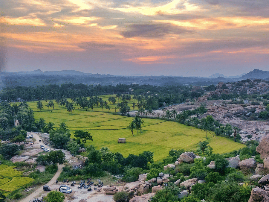 First-person view of blue shoes overlooking a lush green valley and rocky hills during sunset.