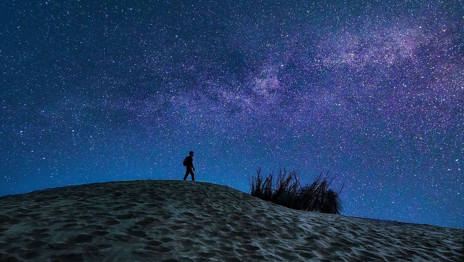 a person walking on the sand dunes of Jaisalmer with stars in the night sky in the background