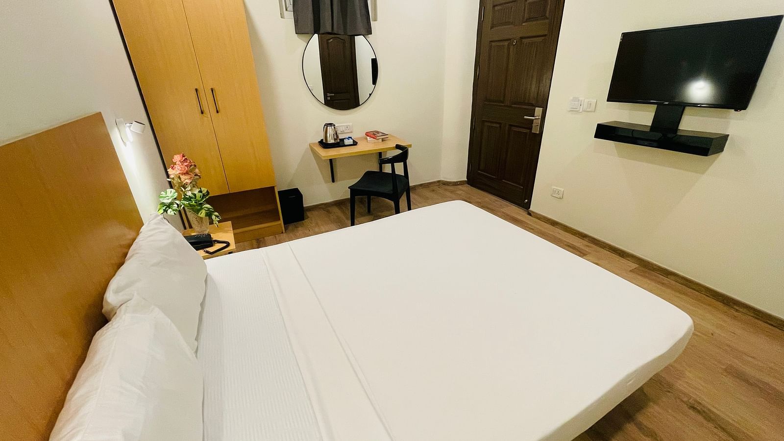 A double bed, a wall-mounted television, a cupboard, and a work desk and a chair at Sanctum Suites Richmond Road, Bangalore.