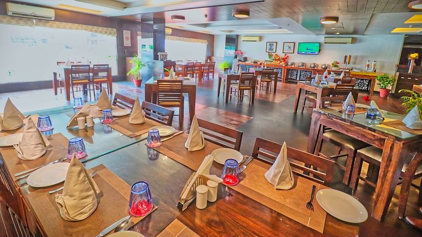 A spacious and well-lit restaurant with wooden tables and chairs, set with plates and cutlery -  Clarks Collection, Vadodara