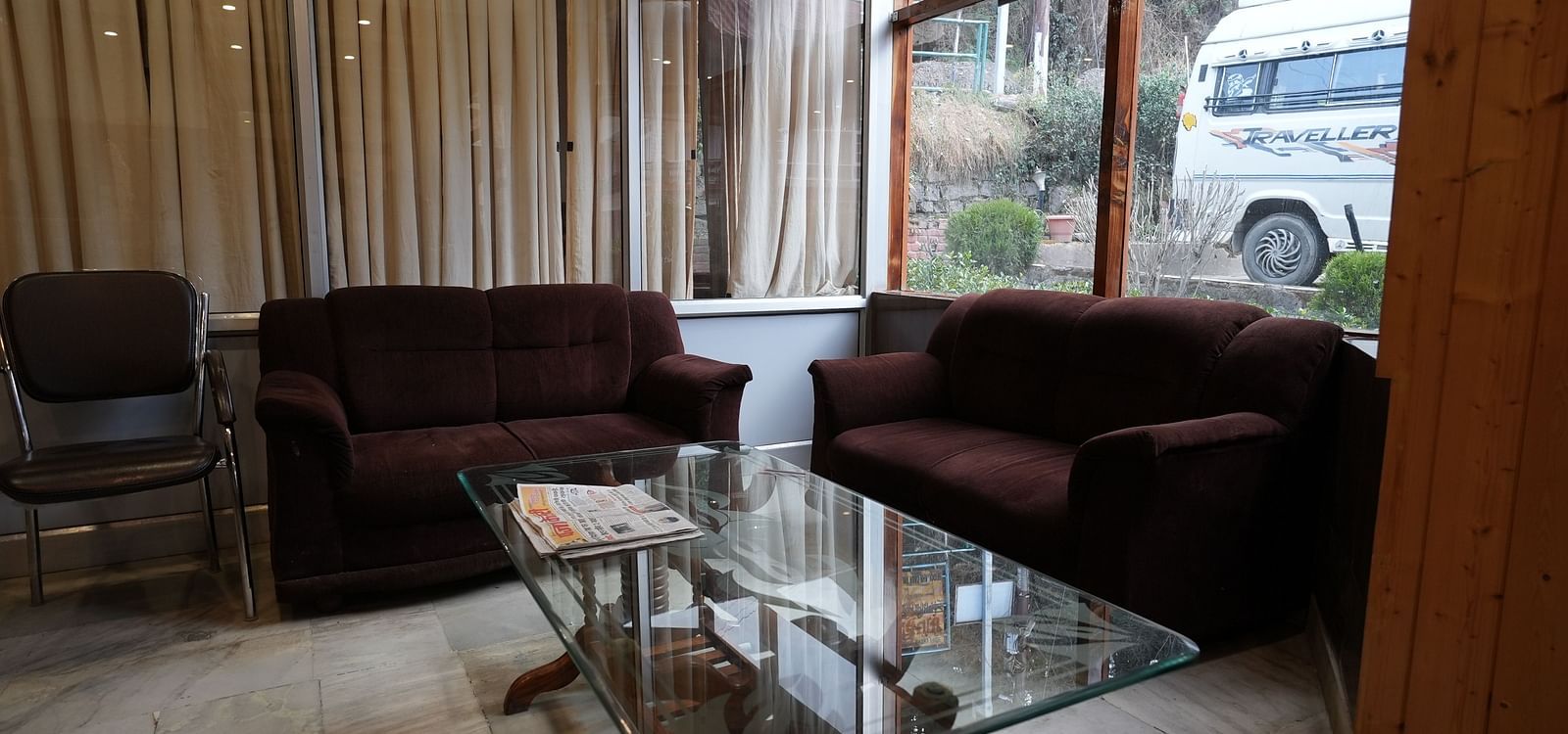 Cozy hotel lounge with plush seating, a glass coffee table, and large windows offering natural light and an outdoor view.