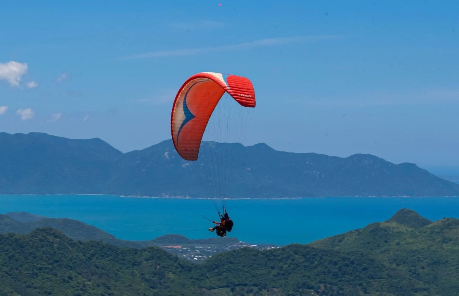 Paraglider soaring over forested hills and blue waters, enjoying scenic coastal