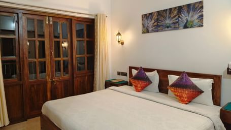 A double bed with colourful pillows and a frame hanging on the wall at 103 room at Ananda Holiday Home, Wayanad 4