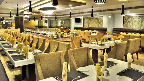 A spacious and elegantly lit restaurant with plush seating, neatly set tables, and a buffet counter – Raj Park Hotel in Alwarpet, Chennai
