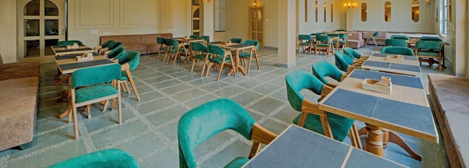 Elegant dining area at Grassfield Riveria Resort, Jaipur, with teal upholstered chairs, wooden tables, and warm lighting.