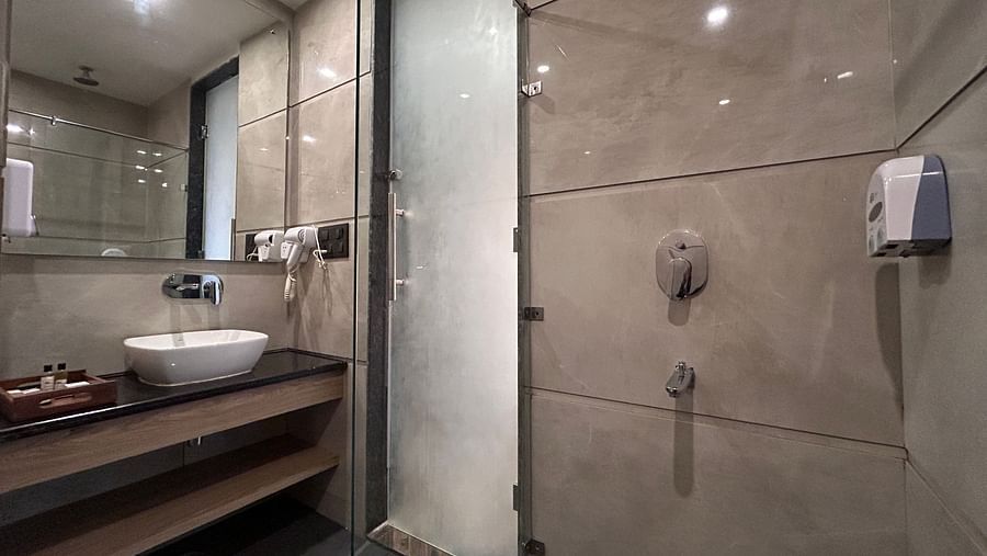 The washroom of the premium room featuring the wash basin, wall mounted mirror, and the shower area - DLS Grand Luxotica, Dehradun