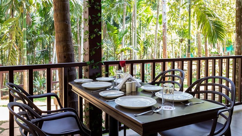 A dining table with plates and cutlery placed on it in an open air restaurant - Stone Wood Nature Resort, Gokarna
