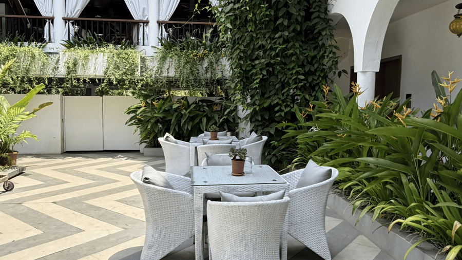 CourtyardOutdoor tables and chairs set on a patterned floor, surrounded by green shrubs, creepers at Bougainvillea, Alibaug.