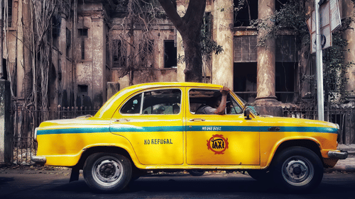 Classic yellow taxi parked beside a heritage building in Kolkata.