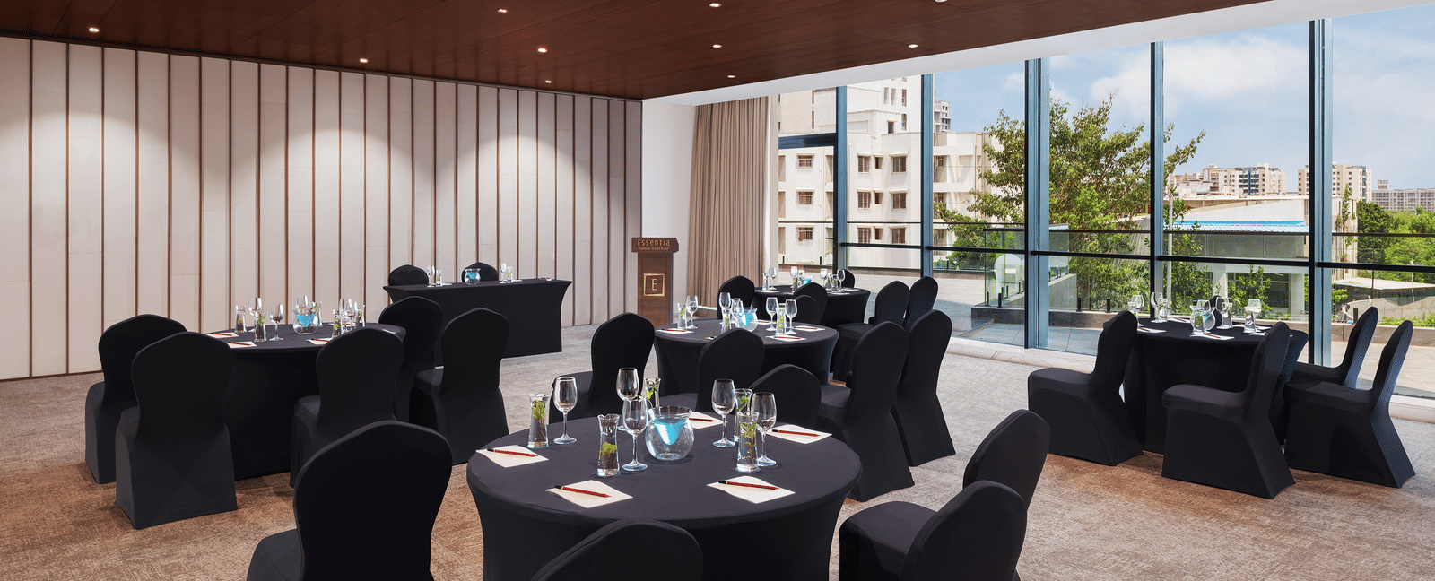 Carnival 1 with tables surrounded with tables at Essentia Premiere, Pune under warm lighting with large ceiling-to-floor windows in the background