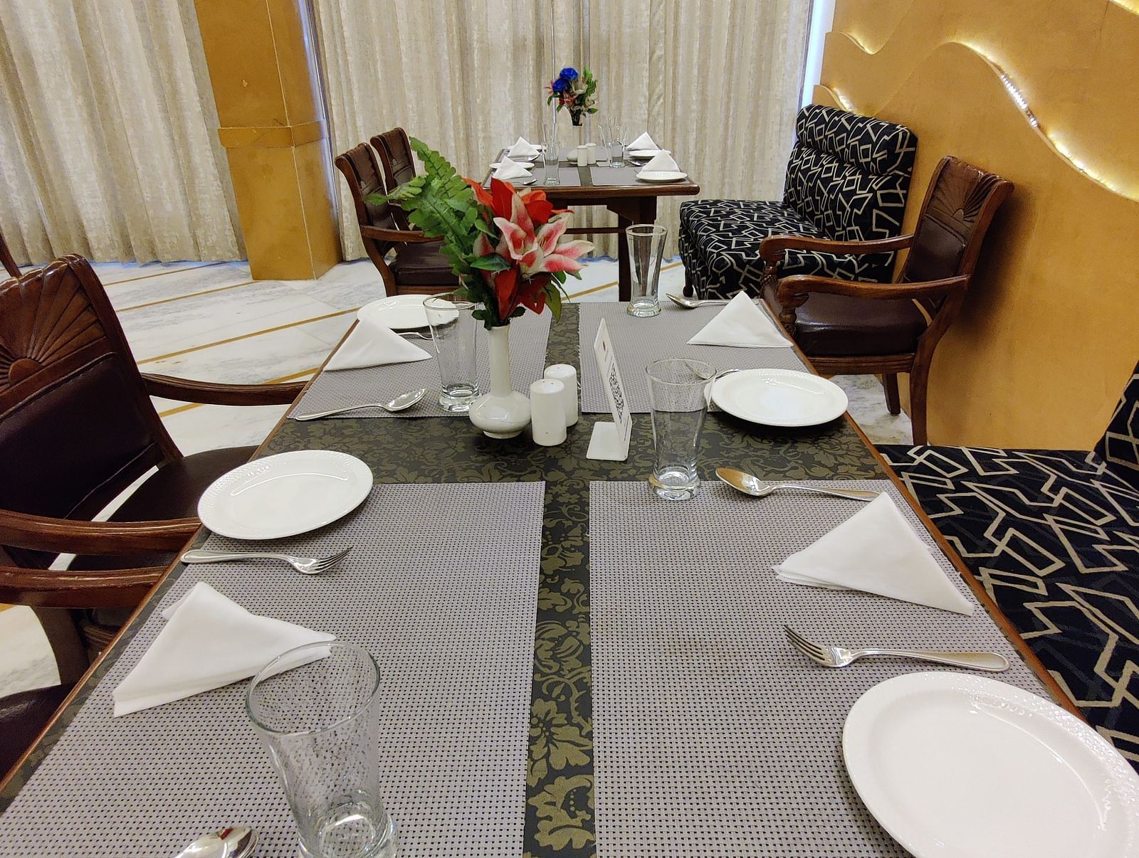 Close up shot of the dining table with table mats and plates along with cutlery and napkins arranged on the table - Hotel Gold, Panipat