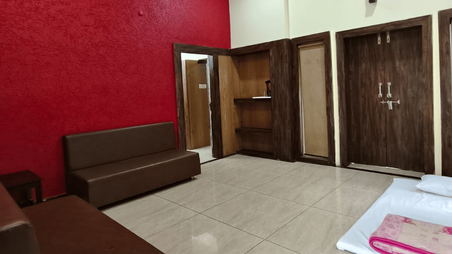 An indoor sitting area with a red accent wall, a large brown sofa, and closed dark wood doors | Nandan Resort