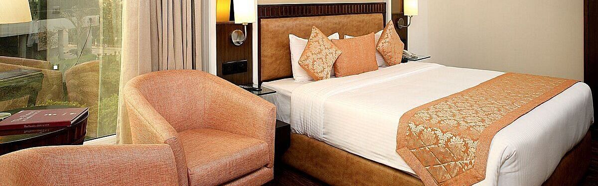 Executive Room with a double bed, bedside table with a lamp on top, cushioned seating with a table in front, and a window behind at Inde Signature Tower, Gurgaon