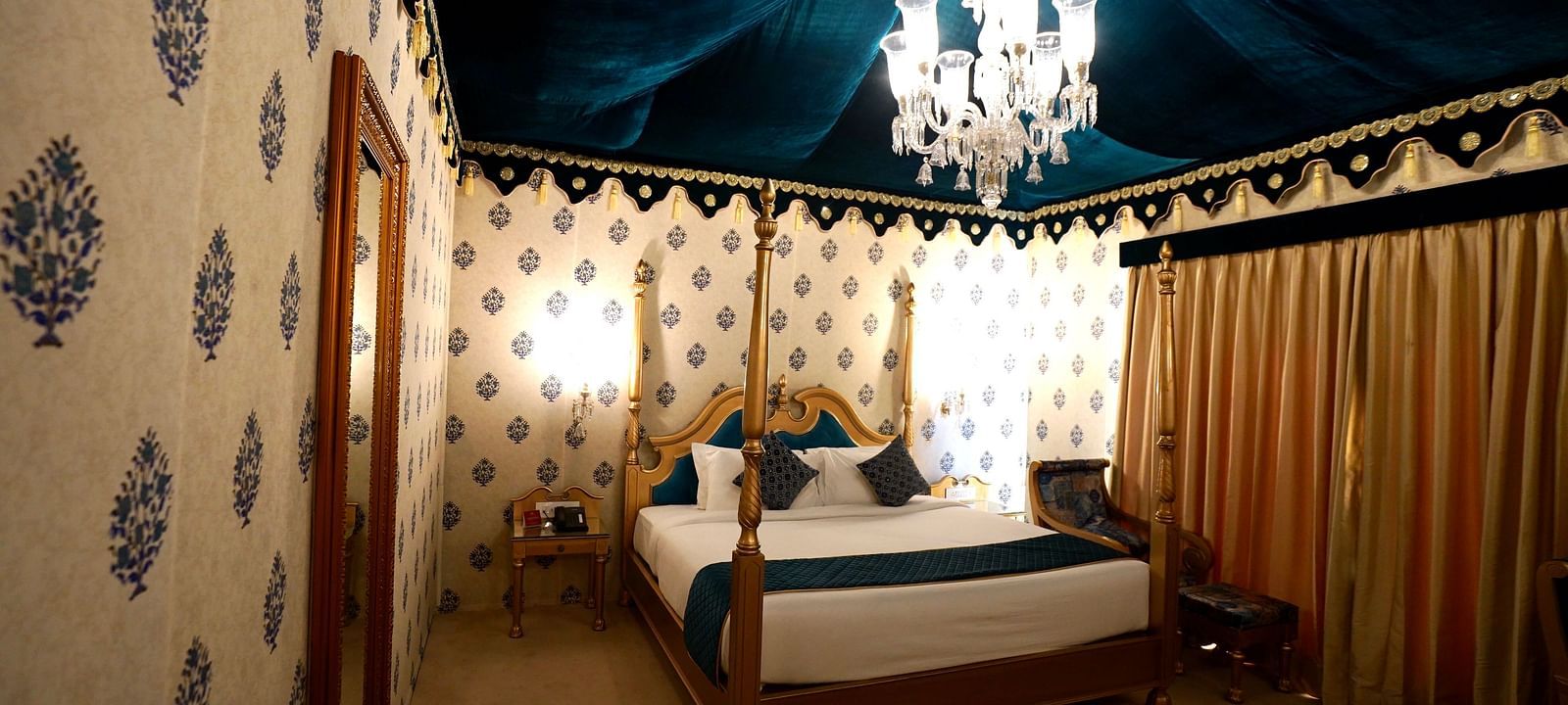 Image of a room with a bed, a mirror on the side and a chandelier hanging from the ceiling.