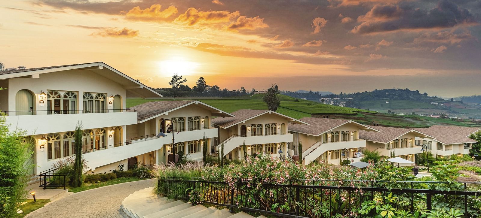 Walkway weaving through Mango Hill Shola, Ooty, flanked by resort buildings and landscaped surroundings.