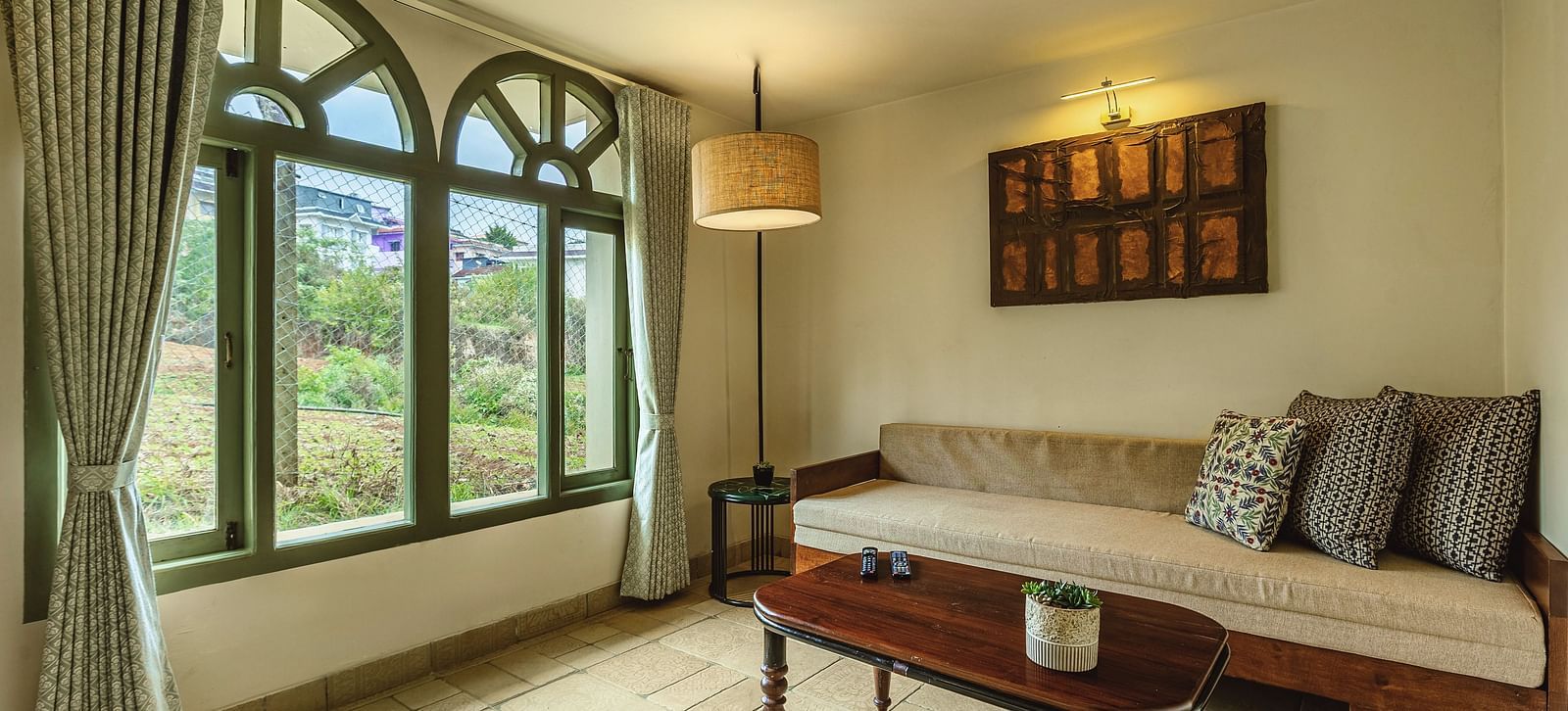 Corner view of a bright room at Mango Hill Shola, Ooty with full-length arched windows, natural light, and a daybed seating nook.