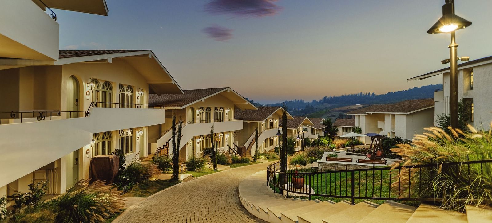 Distant view of a valley near Mango Hill Shola, Ooty, featuring gently sloping hills and scattered buildings.