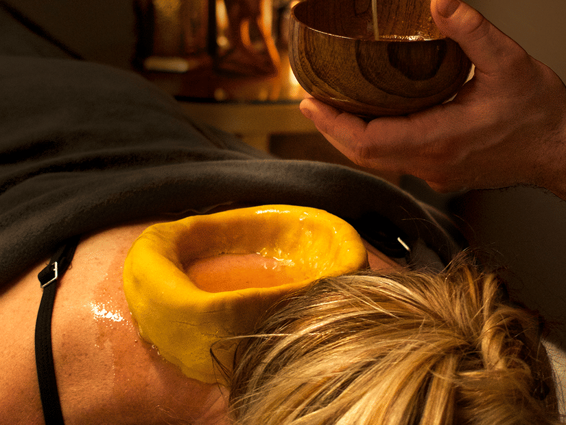 An Ayurvedic treatment being applied to a woman’s back, with warm oil poured into a dough ring.