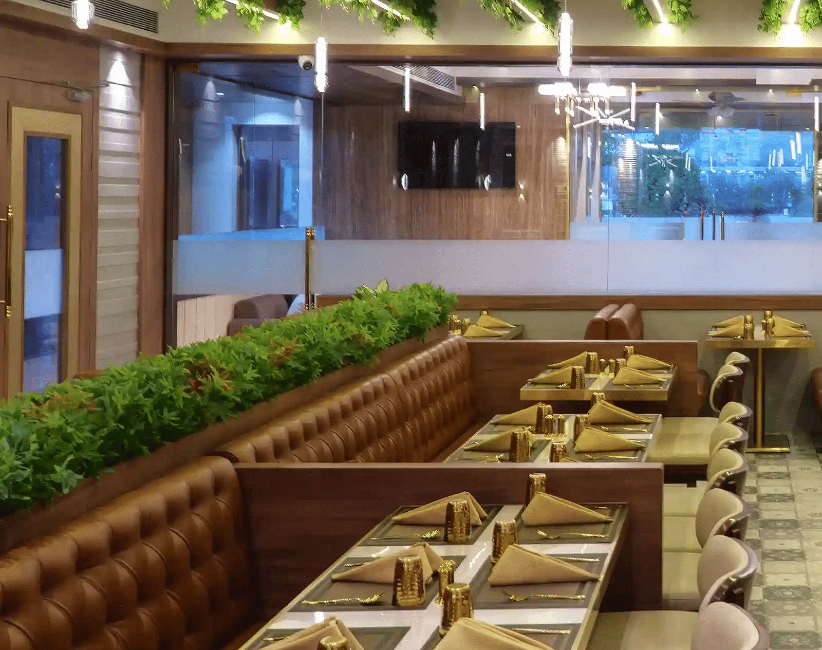 Straight view of dining tables with neatly placed cutlery arranged with glass doors and well-lit and decorated ceiling at Naivedya Restaurant in Melior Inn.