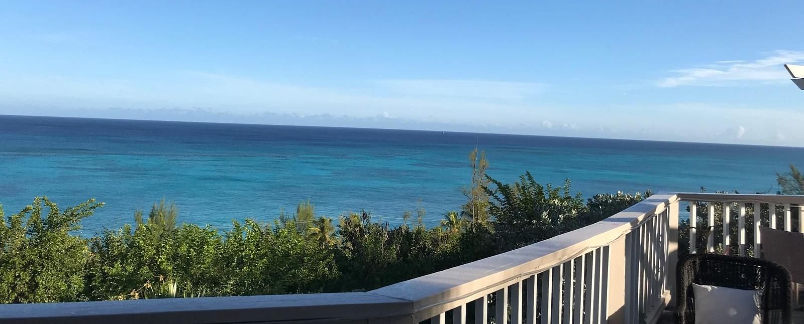 View of the ocean and trees from a deck with a chair and railing | A Stone's Throw Away