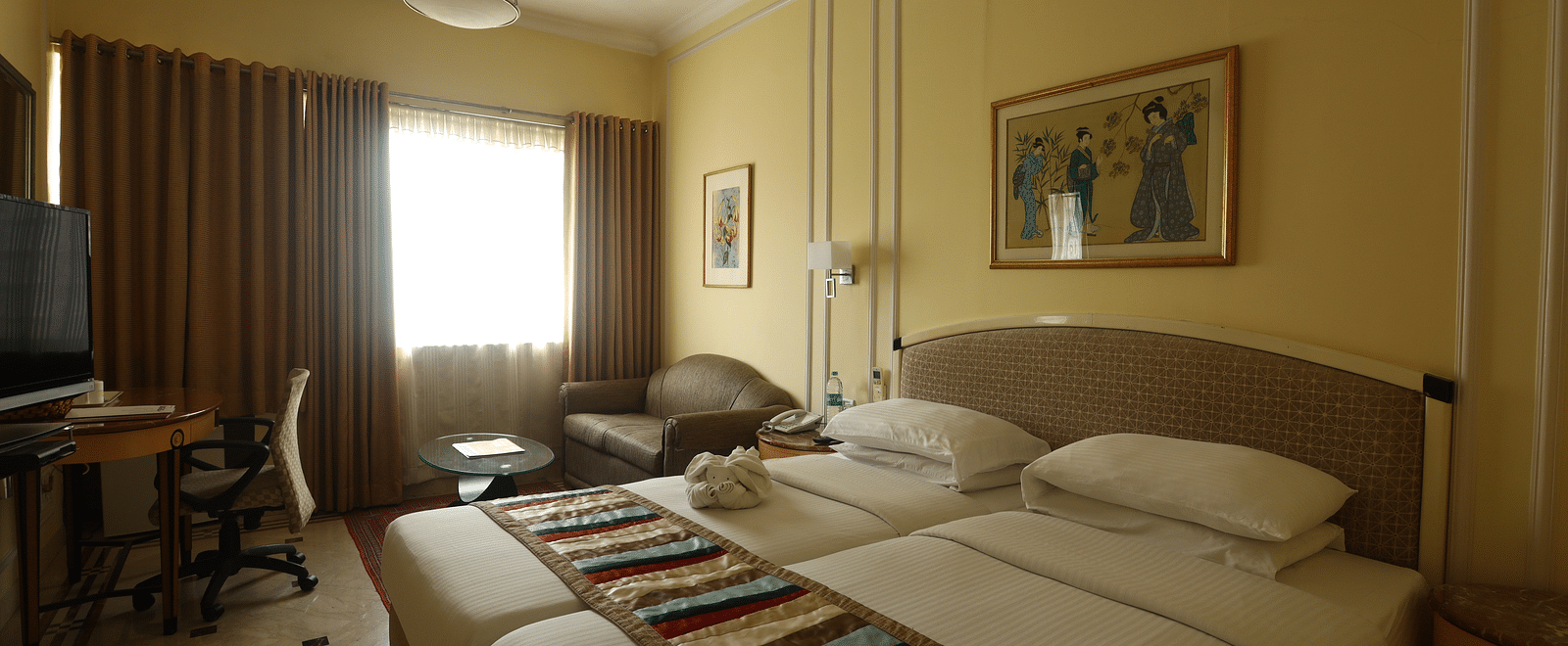 Twin beds in the Superior Room with sunlight peeking through the windows at Regency Hotel, Mumbai.