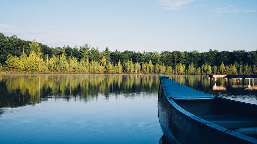an image of a quiet lake surrounded by green trees and corner view of a boat anchored on the lake side