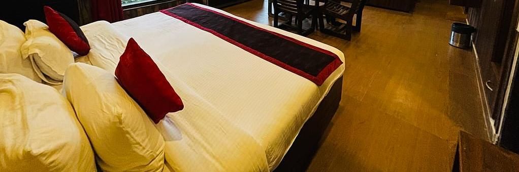 A Family Cottage with beds facing towards each other seperated by a round dining table and TV at DLS MJ River Resort, Rishikesh.