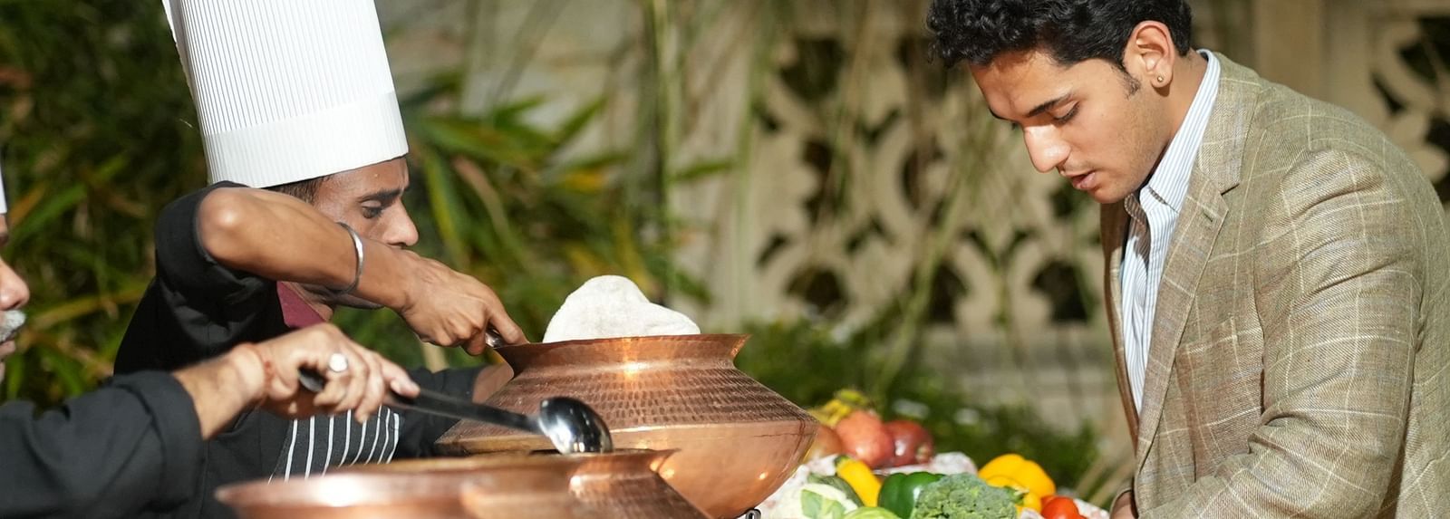 A chef and a guest discuss the menu beside a buffet spread in traditional copper pots - Khas Bagh, Jaipur.