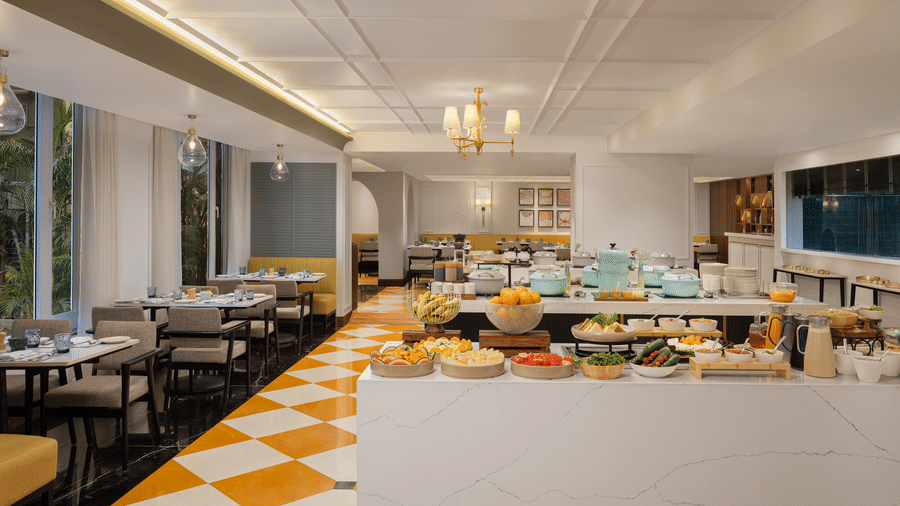 Modern living area with a grey sofa, yellow accent wall, and a large window overlooking a river and mountains.