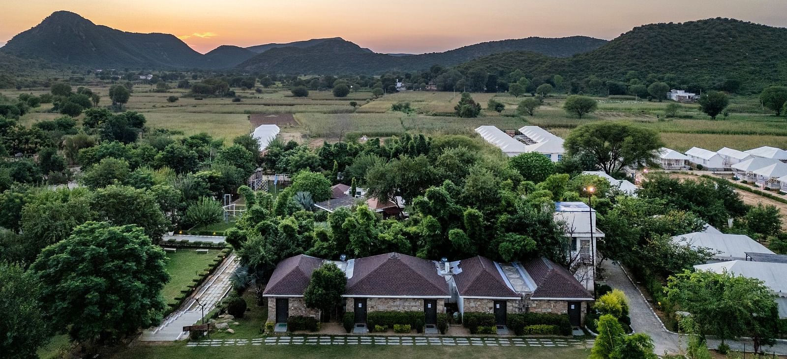 Aerial view of Valley by Grassfield, surrounded by lush greenery with mountains in the background.