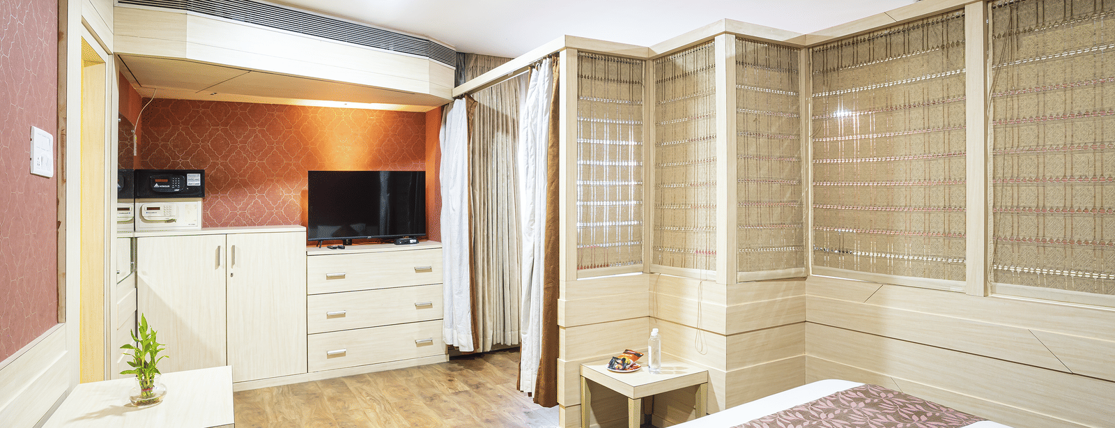 A room with a king size bed, wooden flooring, television and white wardrobe at Infiniti Hotel, Indore.