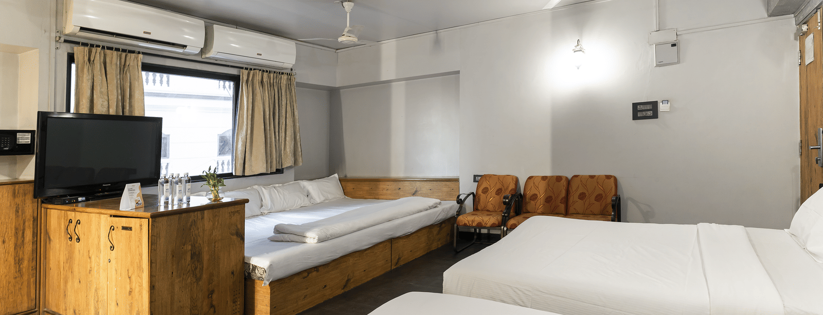 A room with multiple beds, wooden furniture and a television at Infiniti Hotel, Indore.