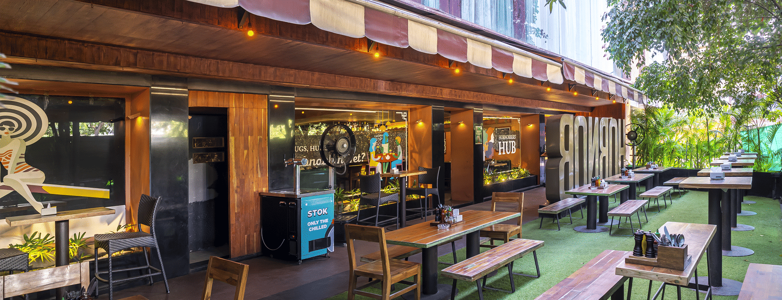 An outdoor seating area with tables, chairs and a long building wall decorated with signs at Infiniti Hotel, Indore.