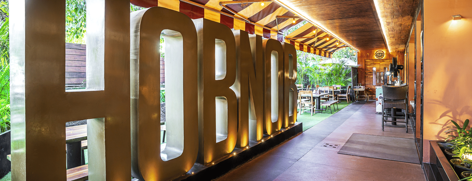 A corridor with large golden letters spelling 'HOBNOB' under a striped canopy at Infiniti Hotel, Indore.