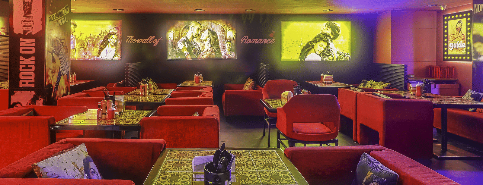 A restaurant interior with red sofas, patterned tables and a glowing signboard reading 'BOLLYWOOD ????' at Infiniti Hotel, Indore.