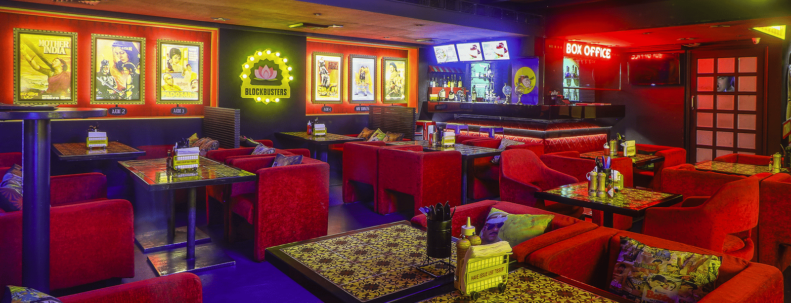 Rows of red sofas and dining tables with framed Bollywood posters and neon lights at Infiniti Hotel, Indore.